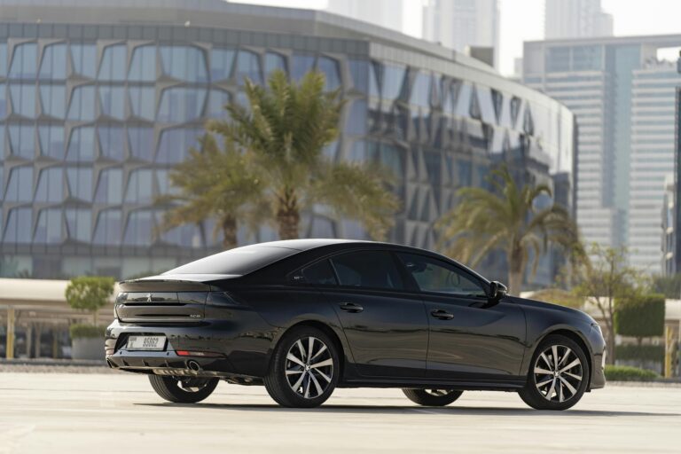 Black Peugeot car parked with Dubai's modern architecture in the background.